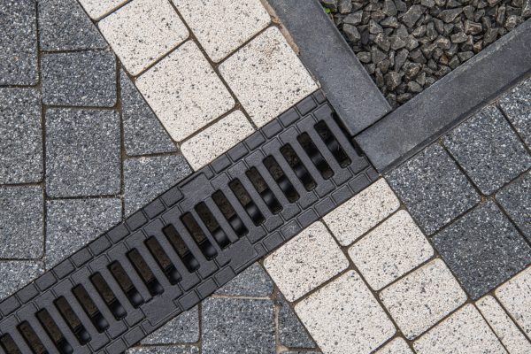 Concrete Bricks in Two Different Colors and Residential Driveway Water Drain Close Up. Architectural Brick Installation Theme.