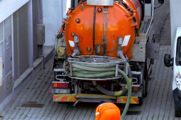 Worker lowers sewer hose into sewer pit.